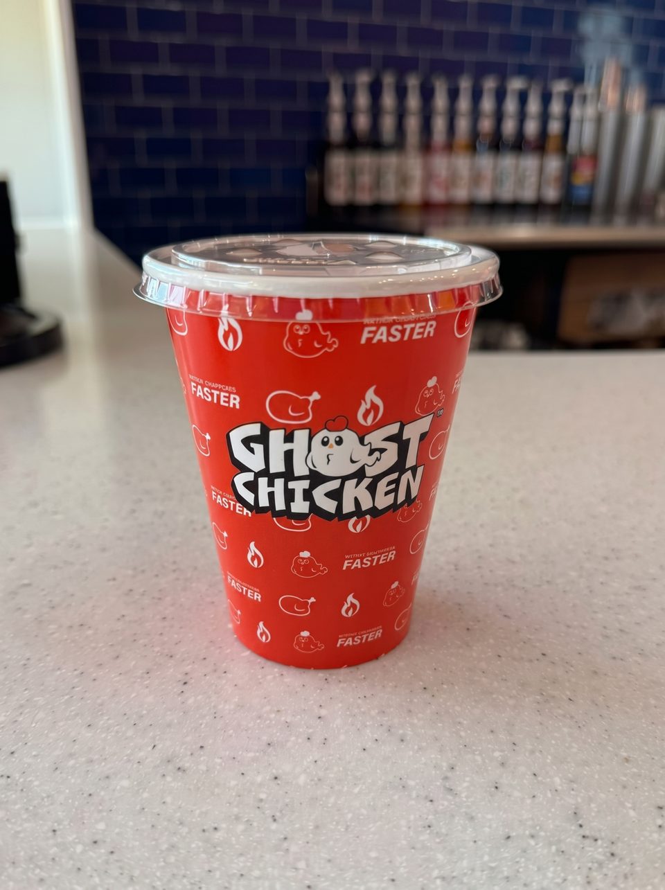 A red Ghost Chicken branded cup with a clear lid sits on a speckled white counter.