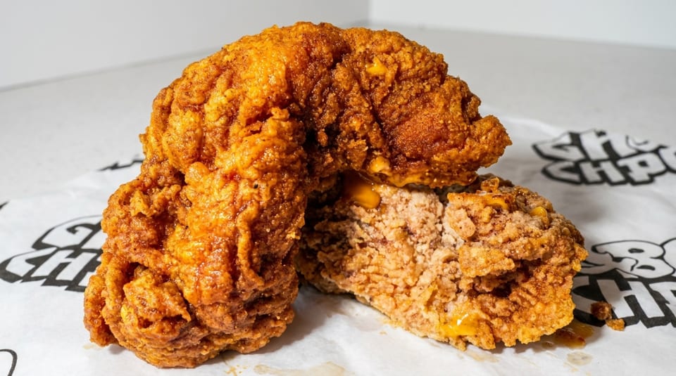 Two pieces of crispy fried chicken, one cut open to show the juicy interior, on branded paper.