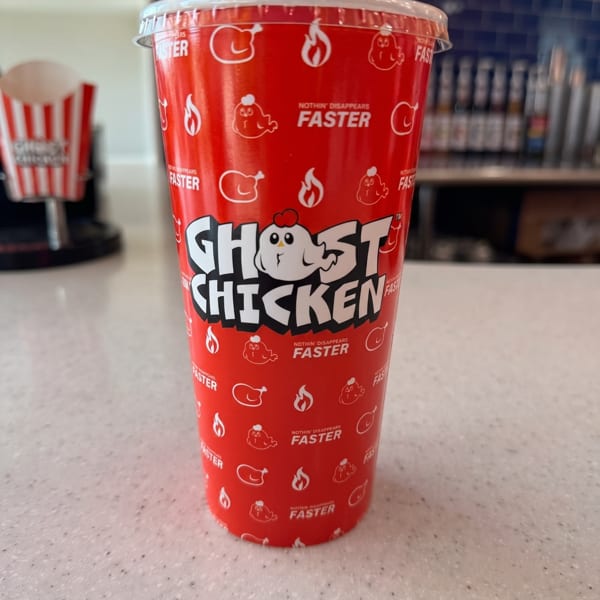 A red Ghost Chicken branded cup with a white lid sits on a speckled white counter.