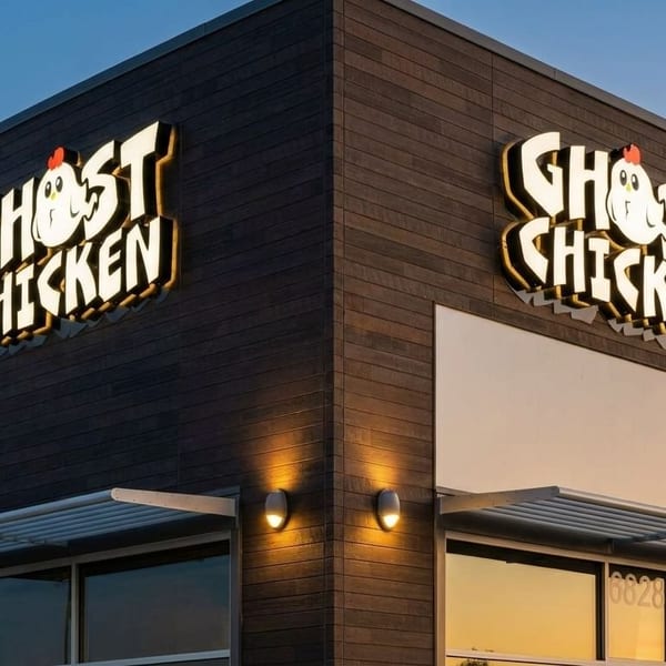 Exterior of Ghost Chicken restaurant with illuminated signs on dark wood paneling at dusk.