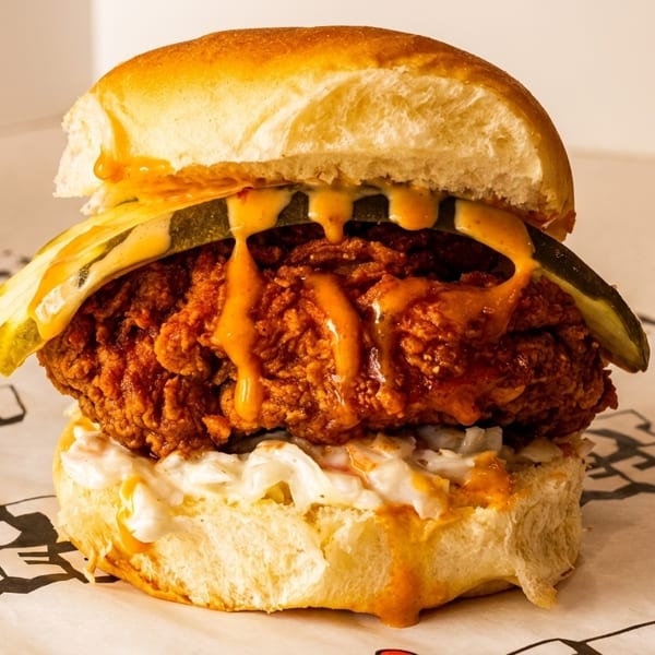 Crispy fried chicken sandwich with pickles, coleslaw, and orange sauce on a bun.