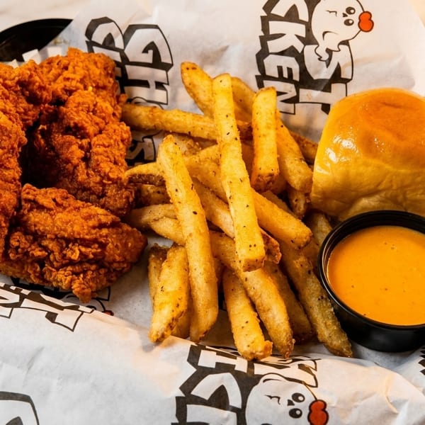 Crispy fried chicken tenders, golden fries, a dinner roll, and dipping sauce in a basket.