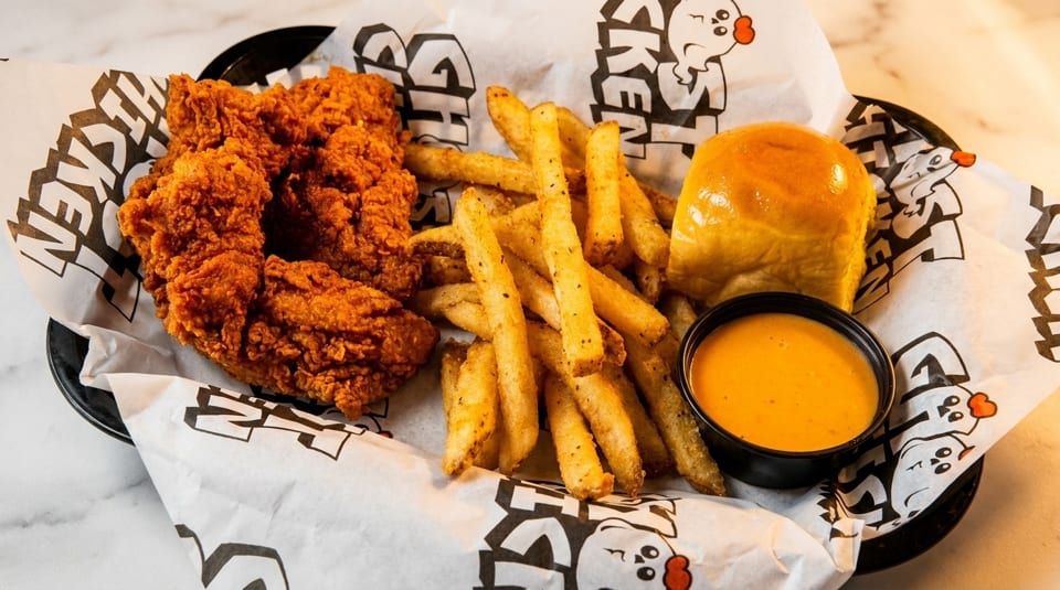 Crispy fried chicken tenders, golden fries, a dinner roll, and dipping sauce in a basket.